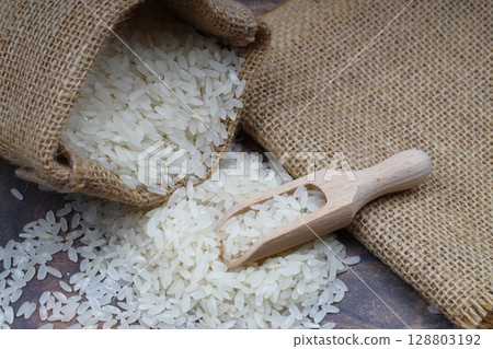 Raw white rice on black background. Long uncooked rice in wooden plate. Natural organic food. Traditional Asian cereal culture. 128803192