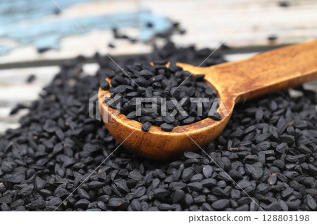 Black cumin seeds and essential oil with bowl and wooden shovel or spoon. Nigella Sativa in glass bottle. Organic herbal medicine for many diseases 128803198