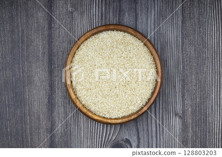 Top view closeup of freshly harvested white sesame in wooden bowl isolated on wooden background with clipping path. 128803203