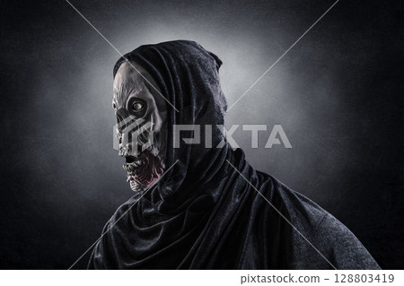 Portrait of a zombie with hooded cape over dark misty background Portrait of a zombie with hooded cape over dark misty background 128803419