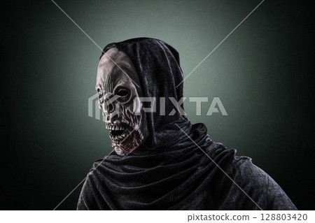 Portrait of a zombie with hooded cape over dark green misty background 128803420