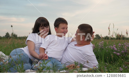 cheerful parent child relaxing green summer meadow, woman man child hugging, happy baby hugs dad outdoors, family hugs, family picnic, father mother with child kid son sunset, little son loves parents 128803681
