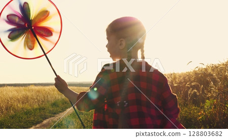 the pinwheel begins to play, child kid runs through park windmill hands, smile face, hand spinning sun, children dream, happy little girl child kid playing with a windmill at sunset, children running 128803682