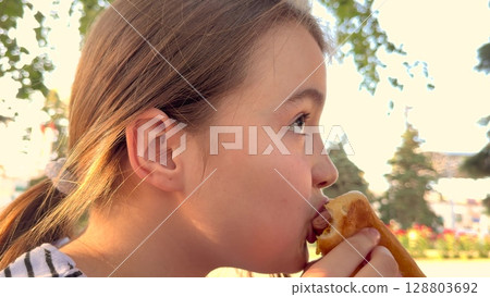 Enjoying summer with a tasty burger, Girl sits in the sunshine, Big bite makes her happy, Her eyes are wide with joy, The park is green and pretty, She loves the fresh air, The burger looks juicy Enjoying summer with a tasty burger, Girl sits in the sunshine, Big bite makes her happy, Her eyes are wide with joy, The park is green and pretty, She loves the fresh air, The burger looks juicy 128803692