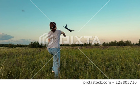 Throwing a plane under clear sky, Young explorer in nature, Imagination takes flight, Flying high with dreams, Serenity in green meadows, Back to nature childhood, Enjoying the simple life, Learning 128803716