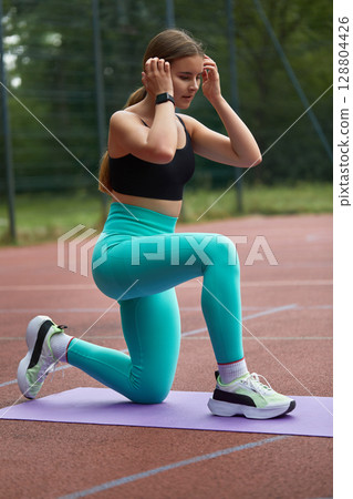Fit woman exercising outdoors on a yoga mat, wearing stylish activewear, showcasing strength and determination in a vibrant setting. Workout concept Fit woman exercising outdoors on a yoga mat, wearing stylish activewear, showcasing strength and determination in a vibrant setting. Workout concept 128804426