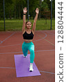 Fit woman exercising outdoors in vibrant activewear, performing a lunge on a yoga mat, showcasing strength and determination in a natural setting. Workout concept 128804444