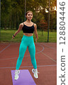 Fit woman exercising outdoors in vibrant activewear, demonstrating strength and agility in a natural environment with copy space. Workout concept 128804446