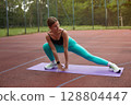 Fit woman stretching on a yoga mat outdoors, showcasing flexibility and strength in a vibrant athletic outfit during fitness routine. Workout concept 128804447