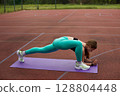 Fit woman stretching on a purple yoga mat outdoors, showcasing flexibility and strength in a vibrant athletic environment. Workout concept 128804448