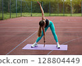 Fit woman stretching on yoga mat outdoors, showcasing flexibility and strength in a vibrant athletic outfit during exercise session. Workout concept 128804449