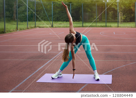 Fit woman stretching on yoga mat outdoors, showcasing flexibility and strength in a vibrant athletic outfit during exercise session. Workout concept Fit woman stretching on yoga mat outdoors, showcasing flexibility and strength in a vibrant athletic outfit during exercise session. Workout concept 128804449