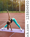 Fit woman practicing yoga outdoors on a purple mat, stretching gracefully in a serene environment, promoting health and wellness. Workout concept 128804450