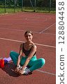 Fit young woman in athletic wear sits on a sports court, surrounded by workout gear, showcasing a relaxed moment after an intense training session, embodying fitness and wellness lifestyle. fit, 128804458