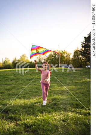 Joyful girl runs with colorful kite in sunny park 128804608
