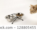 The red cat approaches the metal bowls of dry cat food and water. The concept of food for animals. 128805455