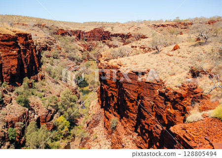 Red rock cliffs and sparse vegetation define Karijini National Park, Australia.. 128805494