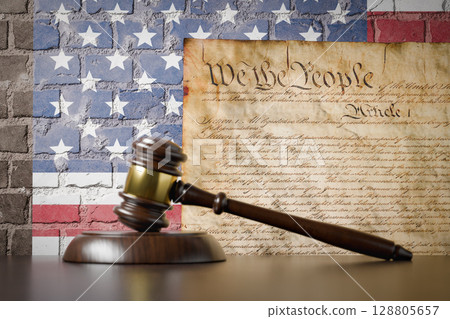 United States Constitution and American Flag On Wall with Gavel Resting on Table in Front. United States Constitution and American Flag On Wall with Gavel Resting on Table in Front. 128805657