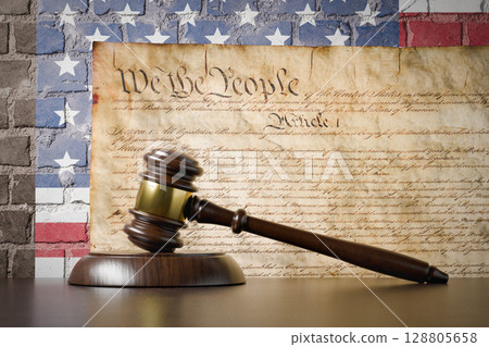 United States Constitution and American Flag On Wall with Gavel Resting on Table in Front. 128805658
