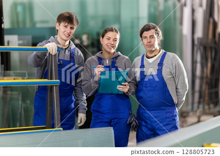Girl and two male glazier employees with documents speaking and advising in workshop 128805723