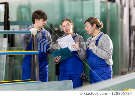 Two men and woman with folder discuss work at glass factory Two men and woman with folder discuss work at glass factory 128805724