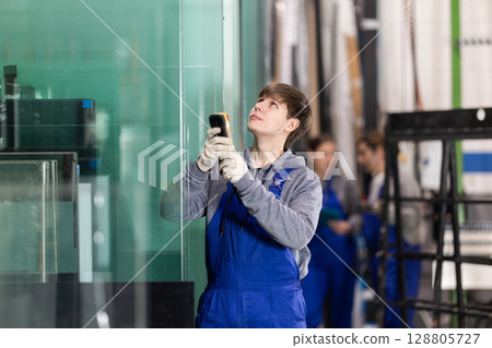 Young man employee in blue overall uses remote control to move lifting mechanism Young man employee in blue overall uses remote control to move lifting mechanism 128805727