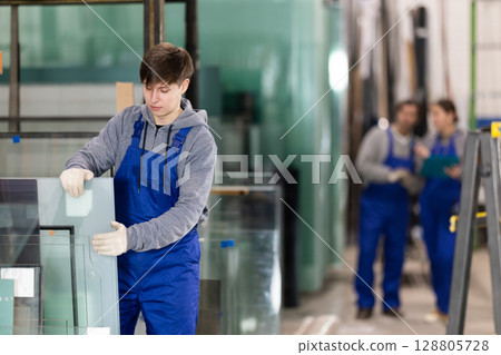 Young guy stacking glass sheets in factory Young guy stacking glass sheets in factory 128805728