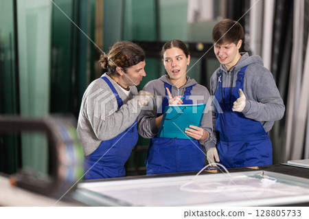 Girl and two male glazier employees with documents speaking and advising in workshop 128805733