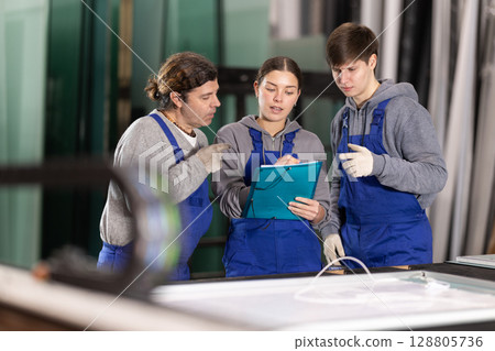 Girl and two male glazier employees with documents speaking and advising in workshop 128805736