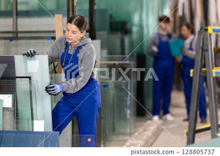 Girl glazer employee in blue overall works in glass processing shop 128805737