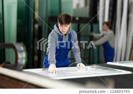 Guy glazer employee in blue overall works in glass processing shop 128805743