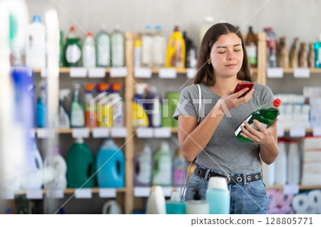 Female shopper using mobile app to pay for dishwashing liquid in store 128805771