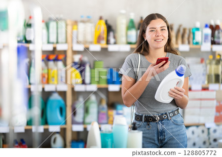 Girl using mobile app to buy detergent in household store 128805772