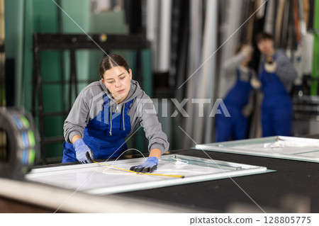 Young woman employee in blue overall measures given length of plastic material Young woman employee in blue overall measures given length of plastic material 128805775