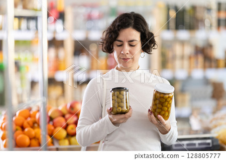 In store, woman near counter are looking at pickled green olives jar In store, woman near counter are looking at pickled green olives jar 128805777