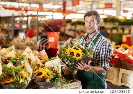 Positive male seller in apron holds designer bouquet in hands 128805828