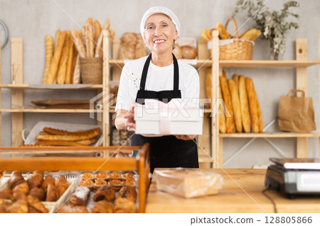 Mature saleswoman holding cake box in bakery Mature saleswoman holding cake box in bakery 128805866