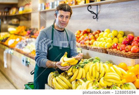 Positive male seller with ripe bananas on supermarket Positive male seller with ripe bananas on supermarket 128805894