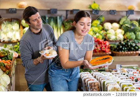 Couple of man and woman buying packaged carrots and sliced papaya in fruit shop Couple of man and woman buying packaged carrots and sliced papaya in fruit shop 128805899