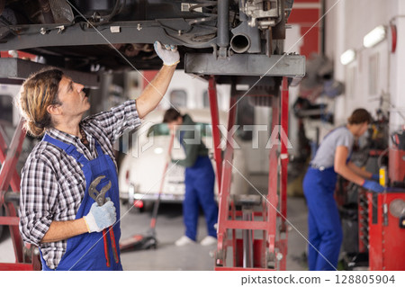 Auto repair shop owner examining undercarriage on car on lift 128805904