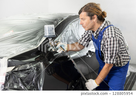 Repairman painter hand in protective glove with airbrush pulverizer painting car body 128805954