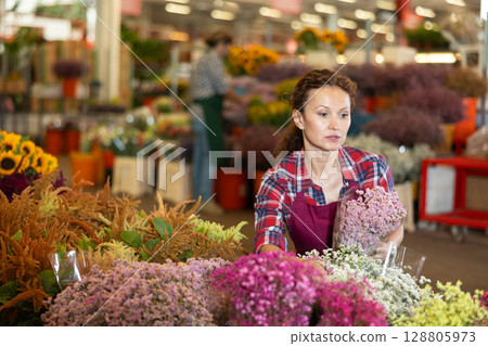 Positive female seller in apron holds dry flowers in hands Positive female seller in apron holds dry flowers in hands 128805973