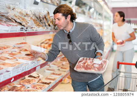 Man shopper chooses fresh meat in the supermarket to cook steak Man shopper chooses fresh meat in the supermarket to cook steak 128805974