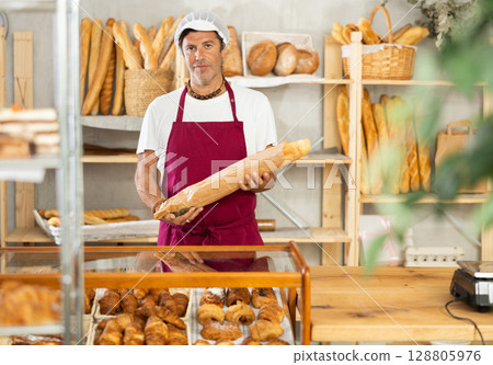 Middle-aged salesman holding paper bag with baguettes in bakery 128805976