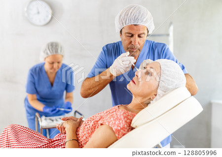 Elderly woman getting injections of hyaluronic acid in cheeks 128805996