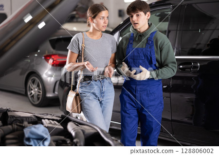 Mechanic advises woman on repairs under hood of car 128806002