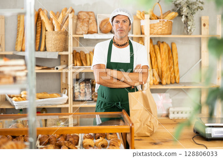 Middle-aged male seller stands in bake house, ready to greet customers 128806033