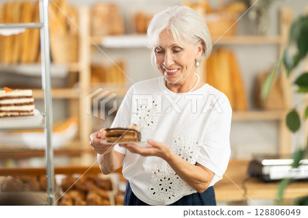 Pleased mature woman holding pastry on paper plate in bakery Pleased mature woman holding pastry on paper plate in bakery 128806049