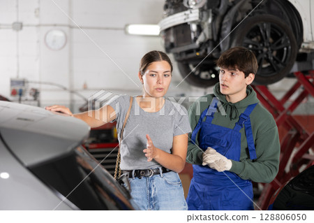 Girl who owns car talks about problems to an auto mechanic at car service center 128806050