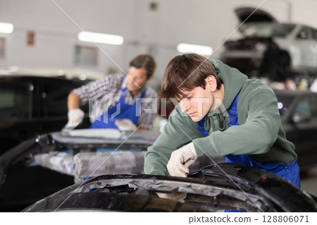 Young auto body technician repairing car bumper in workshop Young auto body technician repairing car bumper in workshop 128806071